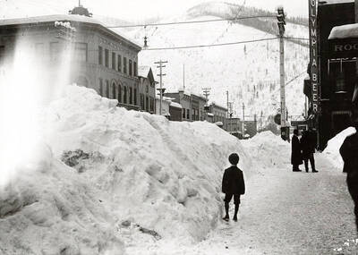 Looking down Cedar Street during the winter in Wallace, Idaho. Residents stand around next to buildings in the snow.