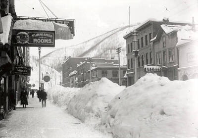 Looking down Cedar Street during the winter in Wallace, Idaho. Residents are walking next to buildings in the snow.