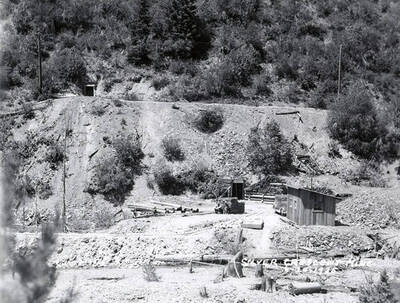 View of Silver Crescent Mine in Kellogg, Idaho. There are two men sitting by a pile of logs.