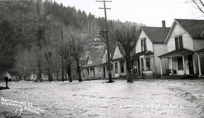 Looking west on Pine Street during the Placer Creek flood in Wallace, Idaho. Houses line the street and some residents can be seen standing on porches.