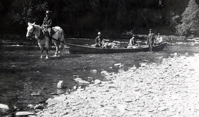 Men sitting in a boat and fishing on the North Fork. One man is sitting on a horse in front of the boat.