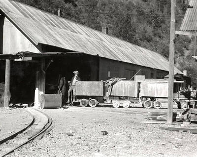 E.E. Gnaedinger standing with ore carts on surface of the Silver Dollar Mine in Osburn, Idaho.