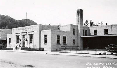 Exterior view of the Post Office in Wallace, Idaho. Two people can be seen walking on the steps.