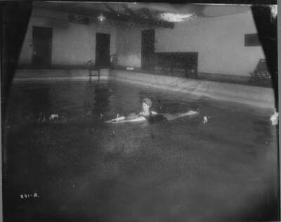 Interior image of the Wallace High School swimming pool. This photo shows several male students posing in diving positions, sitting around and swimming in the pool.