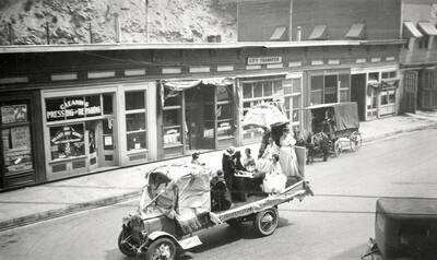 A float, with a table and a group of people sitting around it, being driven in the Fourth of July Parade in Wallace, Idaho.