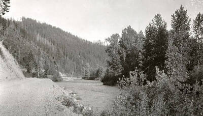 View of the North Fork of the Coeur d'Alene River. Trees line the bank of the river, and a bridge can be seen crossing it.