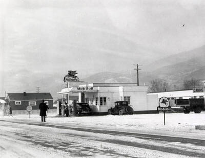Exterior view of the Mobiloil gasoline station in Wallace, Idaho. A man can be seen standing on the street in front of the station. Taken for Keane & McCann, lawyers.