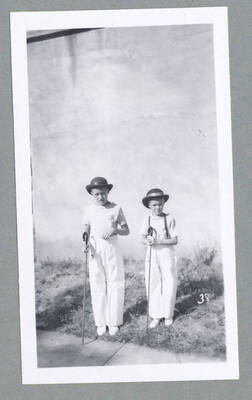 Children in costume walking along during the Children's Parade. The boy in the center is carrying a toy rifle and a small child on his back.