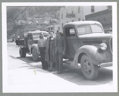 Trucks with first shipment of ore from Silver Cable Mine. Three individuals are posing beside the loaded up trucks.
