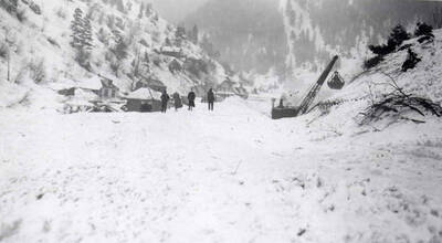 Four people watching a crane remove snow after the snow slide in Mace, Idaho.