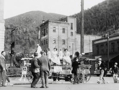 Girls sitting on a float, with men standing next to it during the Elks Roundup parade in Wallace, Idaho.