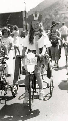 A child, who is in costume, riding a bicycle in the Fourth of July Parade in Wallace, Idaho.