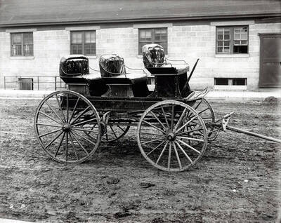 Image shows Henry Floyd Samuels horse drawn carriage located on a muddy road with a building in the background.