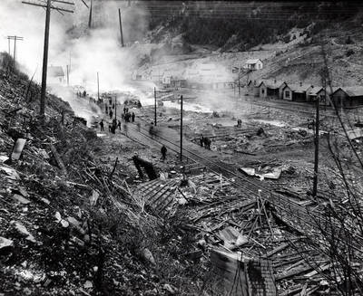 Image is of people walking around the railroad track and among the smoldering debris after a fire in Black Bear, Idaho.