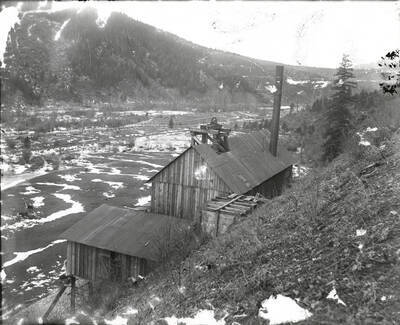 Exterior of the Evolution Mine in Osburn, Idaho, taken from above. A distant horse and buggy can be seen in the field.