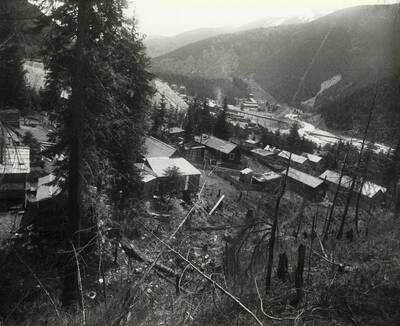 Slaughterhouse Gulch in Mullan, Idaho looking South East. The Morning Mill waste rock pile is to the left and Tennis Row housing in the upper middle of the picture. Note the flume line from the Morning Mill dumping directly into the South Fork of the Coeur d'Alene River