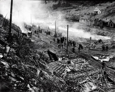 Image is of people walking around the railroad track and among the smoldering debris after a fire in Black Bear, Idaho.