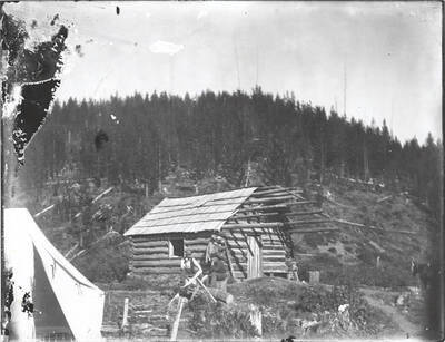 Men seated around a fire pit outside of a cabin. The name "R.K. Stevenson" is written on the back of the photograph.
