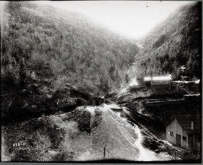 View of a portal for the Standard Mine. A little cabin stands uphill, with a larger wooden building below. Caption from front: "Distant view of entrance."