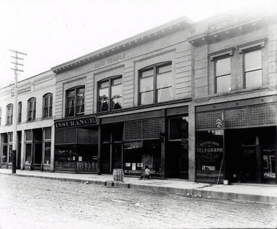 Views of the Elks Temple, Herman J. Rossi Insurance, Western Union and other offices. An unidentified child sits in front of the Elks Temple facing the window.