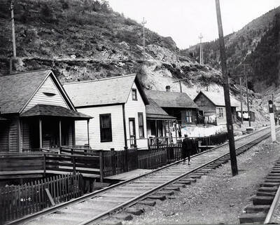 A view of railroad track going through the center of the town of Black Bear, Idaho. A horse and wagon are pictured as well as people walking through town.