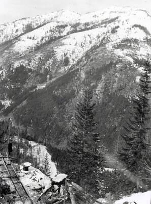 Mountain snow scene of a man standing at the edge of a cliff with mining equipment around him.