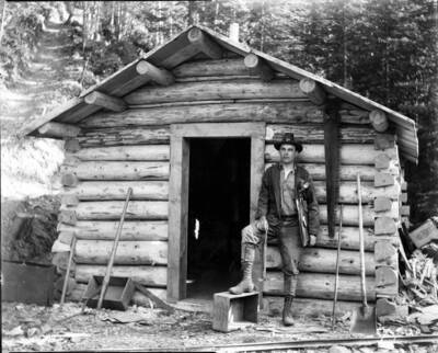 Greenough, W.Earl standing outside of a cabin