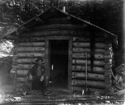 Greenough, W.Earl sitting outside of a cabin