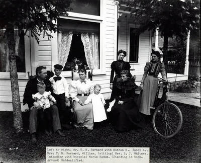 Image shows T.N. Barnard at his residence in Wallace, Idaho [1898] with a group of people. Mr. Barnard was a photographer and the owner of Barnard's Studio in Wallace, Idaho. Caption below image: "Left to right - Mr. T. N. Barnard with Nathan N., Enoch A., Mrs. T.N. Barnard, William, (sitting) Mrs. L.J. Whitney, (standing with bicycle) Marie Hedum. (Standing in background) Unidentified."