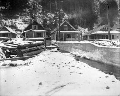 A cement wall on the right keeping the stream from flooding and in the back are four houses