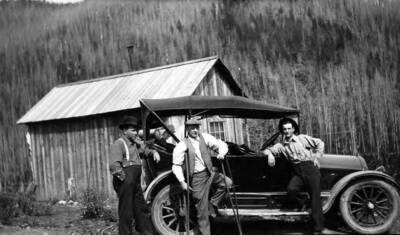 Group of men standing by a car.