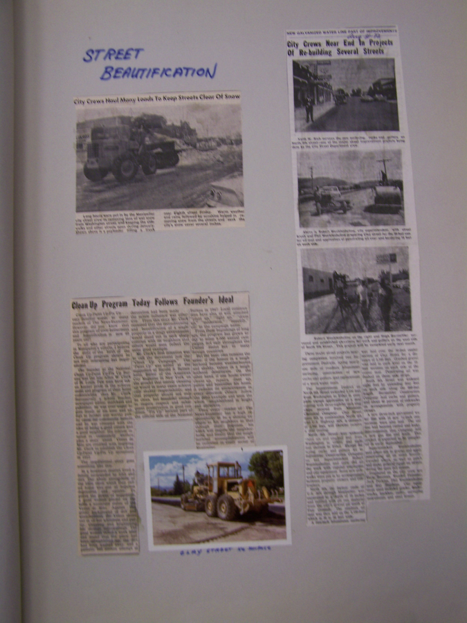 A page titled "Street Beautification" features a collection of three newspaper clippings and one photograph. The first clipping, with a headline about city crews keeping streets clear of snow, includes a picture of machinery working on snowy streets. Beside it is a vertical clipping discussing city crews nearing the end of street rebuilding projects, with two images of streets and vehicles. Below is a lengthy article titled "Clean Up Program Today Follows Founder's Ideal" with no accompanying image. At the bottom, a photo shows a large street grader on a road labeled "STREET GRADER IN MOTION."