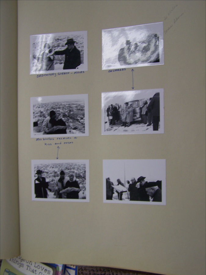 A page displaying six small images arranged in two columns. The top left image shows a person giving a speech labeled "DEDCATOR'S SPEECH - MILES." The top right image depicts several people with the label "ON LOOKERS." The middle left image shows a couple looking out over a cityscape, labeled "Mrs. Winters receives a kiss and roses." On the middle right, people gather around a vehicle. The bottom left image features people standing and interacting, while the bottom right image shows a group reading documents. There is handwritten text on the right side and a partial book visible at the bottom left corner.