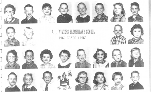 A grid of individual portraits featuring young children and one adult, likely teachers and students, arranged in four rows. The middle of the image contains text that reads "A. J. Winters Elementary School 1962 Grade 1 1963." Below the third row, there is a simple illustration of an inkwell and quill. The children have various hairstyles and outfits, some wearing glasses, and display a range of expressions.