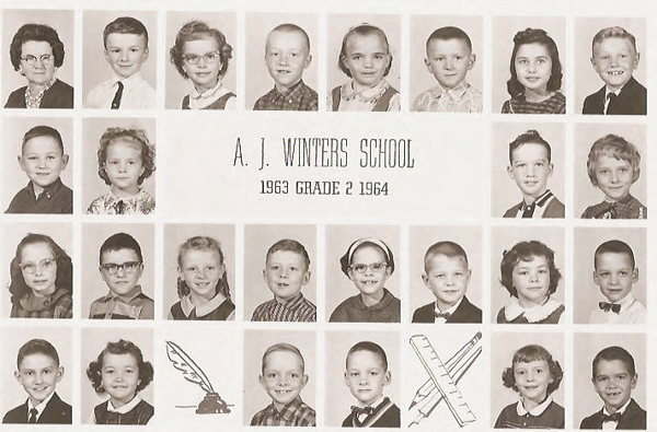 A group of young children and a woman arranged in individual portrait squares. The central text reads "A. J. Winters School, 1963 Grade 2 1964." Below the portraits, there are illustrations of a quill, a pair of compasses, a ruler, and a pencil.