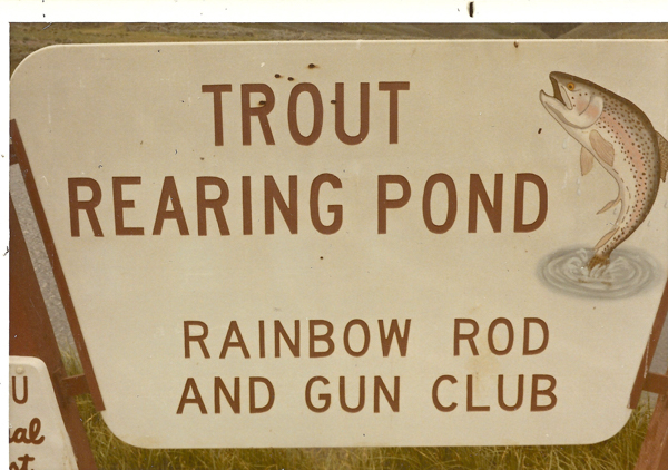 A sign with the text "TROUT REARING POND" and "RAINBOW ROD AND GUN CLUB." There is an illustration of a jumping trout on the right side.