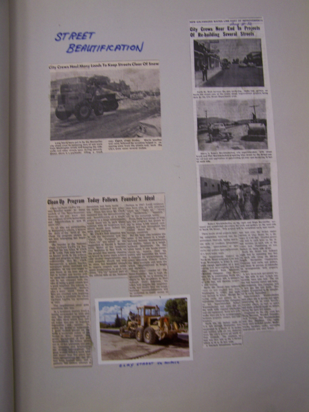 A page titled "Street Beautification" features a collection of three newspaper clippings and one photograph. The first clipping, with a headline about city crews keeping streets clear of snow, includes a picture of machinery working on snowy streets. Beside it is a vertical clipping discussing city crews nearing the end of street rebuilding projects, with two images of streets and vehicles. Below is a lengthy article titled "Clean Up Program Today Follows Founder's Ideal" with no accompanying image. At the bottom, a photo shows a large street grader on a road labeled "STREET GRADER IN MOTION."
