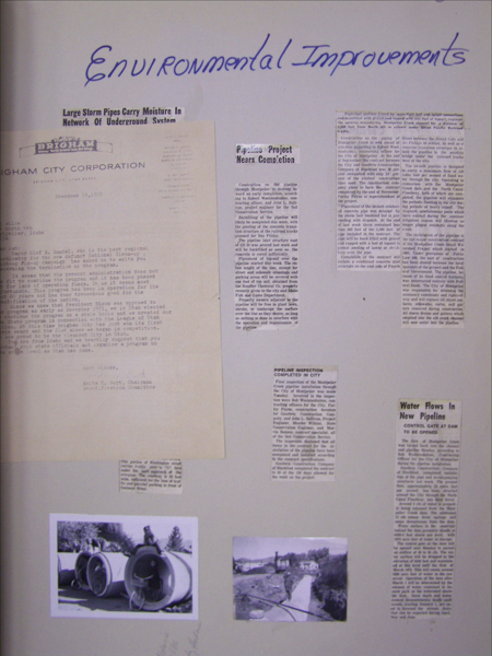 The image shows a collection of documents and photographs mounted on a surface. At the top, there is handwritten text that says "Environmental Improvements." Below, there are several newspaper clippings with headlines such as "Large Storm Pipes Carry Moisture In Network Of Underground System," "Pipeline Project Nears Completion," "Pipeline Inspection Completed In City," and "Water Flows In New Pipeline." There is also a letter from Brigham City Corporation dated November 15, 1952. Two photographs are visible at the bottom; one shows a person sitting inside a large pipe, and the other depicts a landscape with a pipeline under construction.