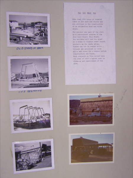 A collection of six small images is displayed on a board alongside a typed document. The images depict various stages of a construction project, with people working with timber and various structures visible. The document, titled "The 3rd Ward Hub," describes the project involving over 1000 hours of donated labor by LDS Church men for building a food and drink stand. It discusses the larger improvement program for Bear Lake County Fair Board, detailing the use of local timber and mills. Handwritten captions under the images include "OLD STAND IN BACK" and "THE BEGINNING." An additional note reads "3rd Ward Hub."