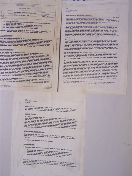Three pages of typewritten text are arranged on a surface. The text includes titles such as "INSPECTION REPORT" and "Description of the Cleanup Operation." The document appears to detail a maintenance operation inspection in Bear Lake County, Idaho, dated 5/12/72. The text discusses a cleanup operation involving students and mentions costs, effectiveness, and observations regarding littering behavior.