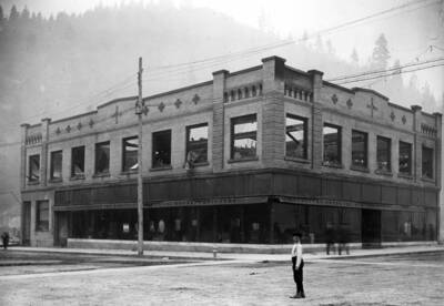 Image shows damage from the forest fire to the Worstell Co. Store. A young boy stands in the intersection looking back at the camera. Forest fire 1910.