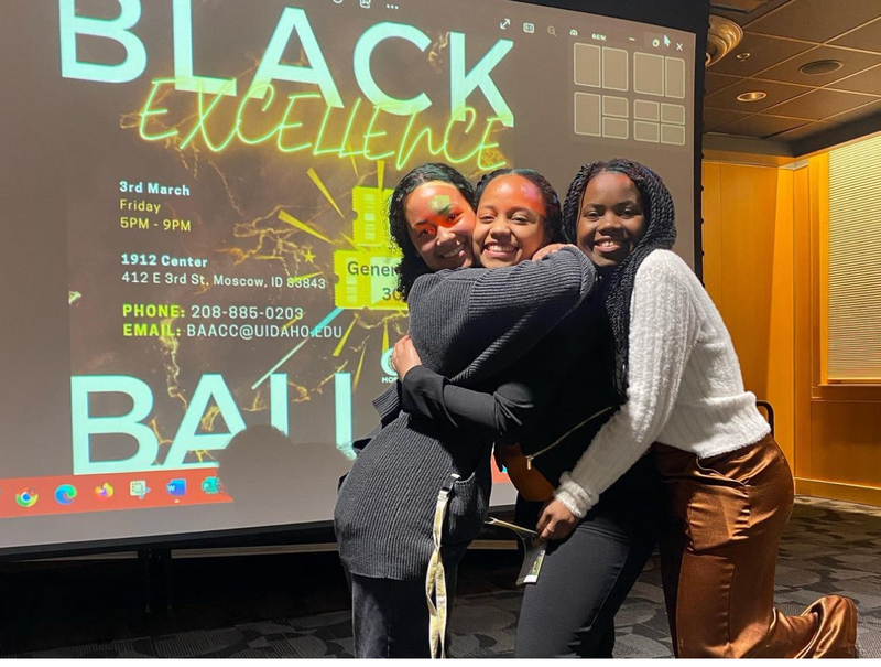 BSU students (Rim Tekle, Reine Byamungu) in front of a projector screen with the Black Excellence Ball post.