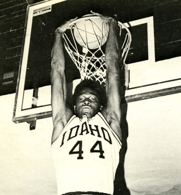 Mickey Brown holding onto the basketball hoop after making a shot.