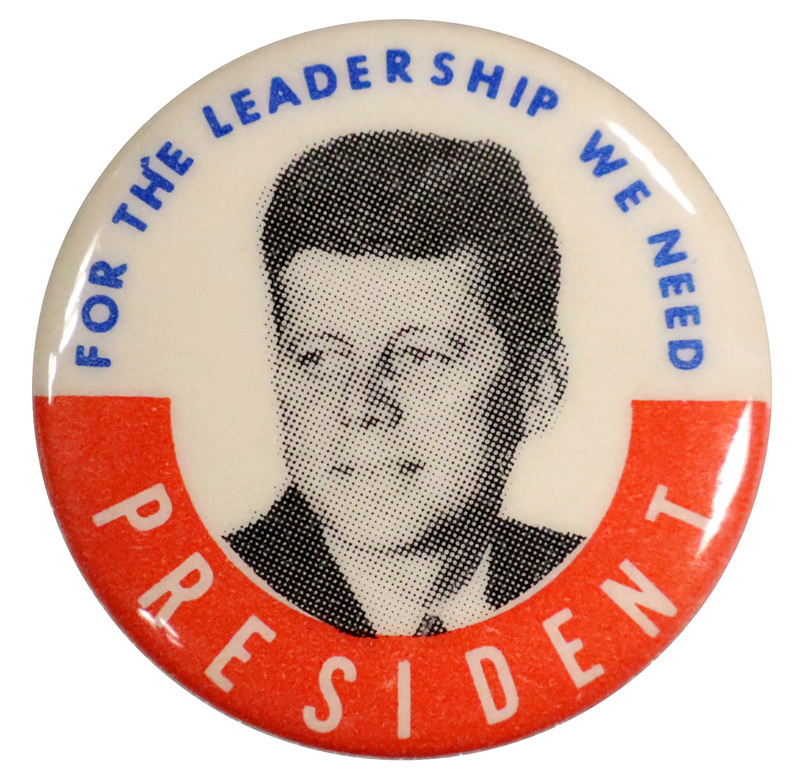 Round, white button with a red border on the bottom half, and a grayscale portrait of John F. Kennedy. Text reads "For the leadership we need President". 