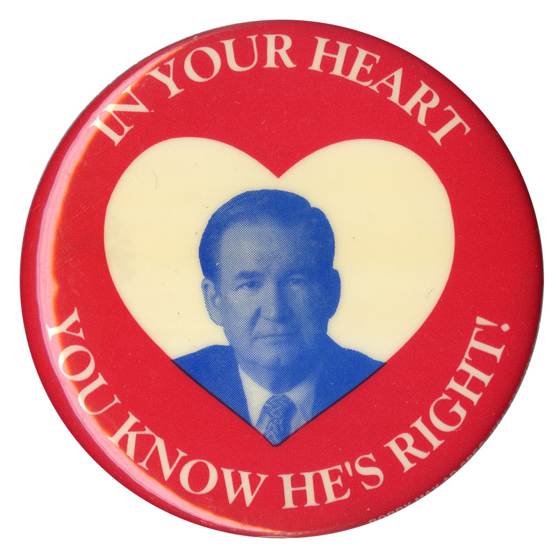 Round, red button with a white heart at the center and a grayscale portrait of Pat Buchanan within it. White text reads "In Your Heart You Know He's Right!" and encircles the portrait. 