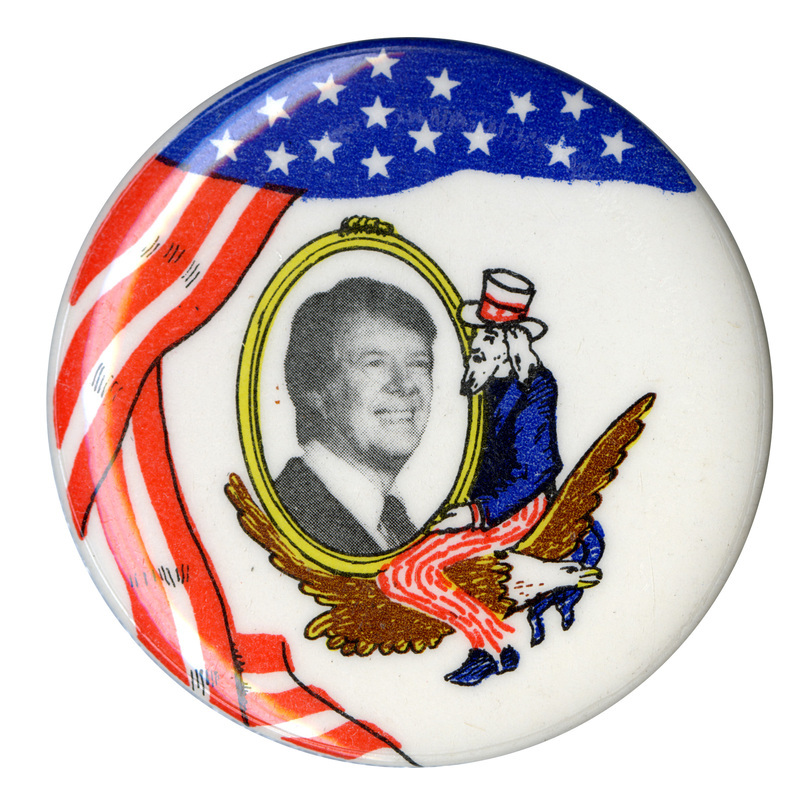 Round, white button with a red, white, and blue drawing of the US flag and a drawing of Uncle Sam sitting on an eagle and cradling an oval that contains a black and white photograph of Jimmy Carter.