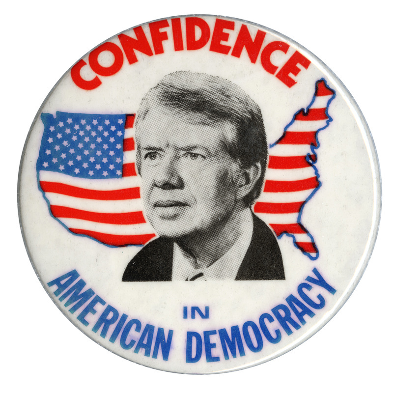 Round, white button with a black and white photograph of Jimmy Carter against a red, white, and blue drawing of the United States filled in by the flag's stars and stripes. Blue and red text reads "CONFIDENCE IN AMERICAN DEMOCRACY"