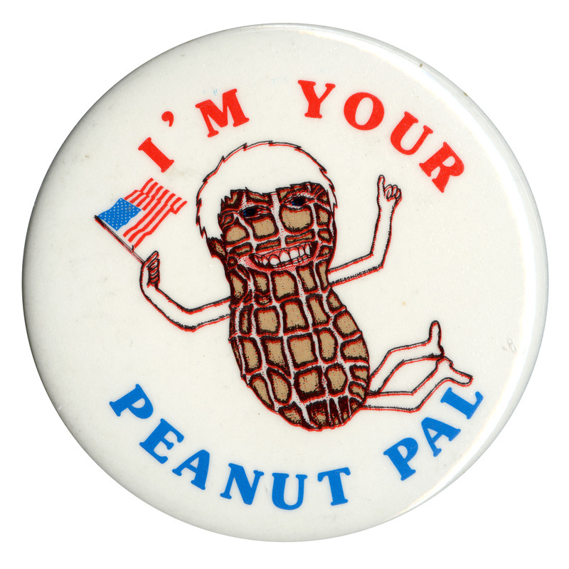 Round, white button with a color drawing of a peanut with arms, legs, hair, and a face, holding a US flag. Red and blue text reads "I'M YOUR PEANUT PAL"