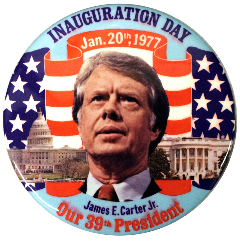 Round button with a color photograph of Jimmy Carter against color photographs of the US Capitol building, the White House, and a US flag. Red, white, and blue text reads "INAUGURATION DAY Jan. 20th, 1977 James E. Carter Jr. Our 39th President"