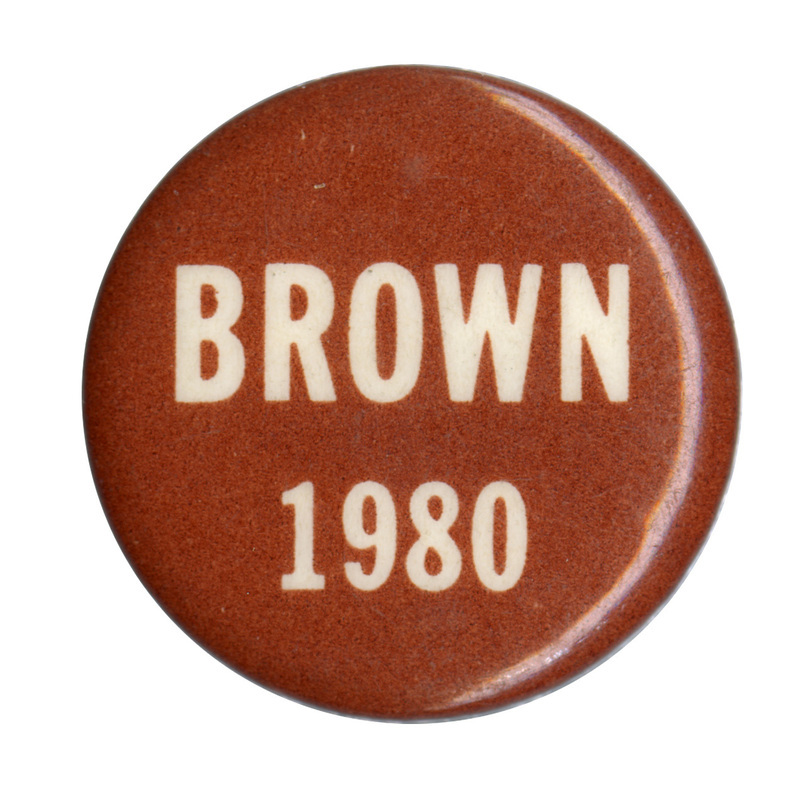 Round, brown button with a white band across the center. Red and white text reads "BROWN 1980"